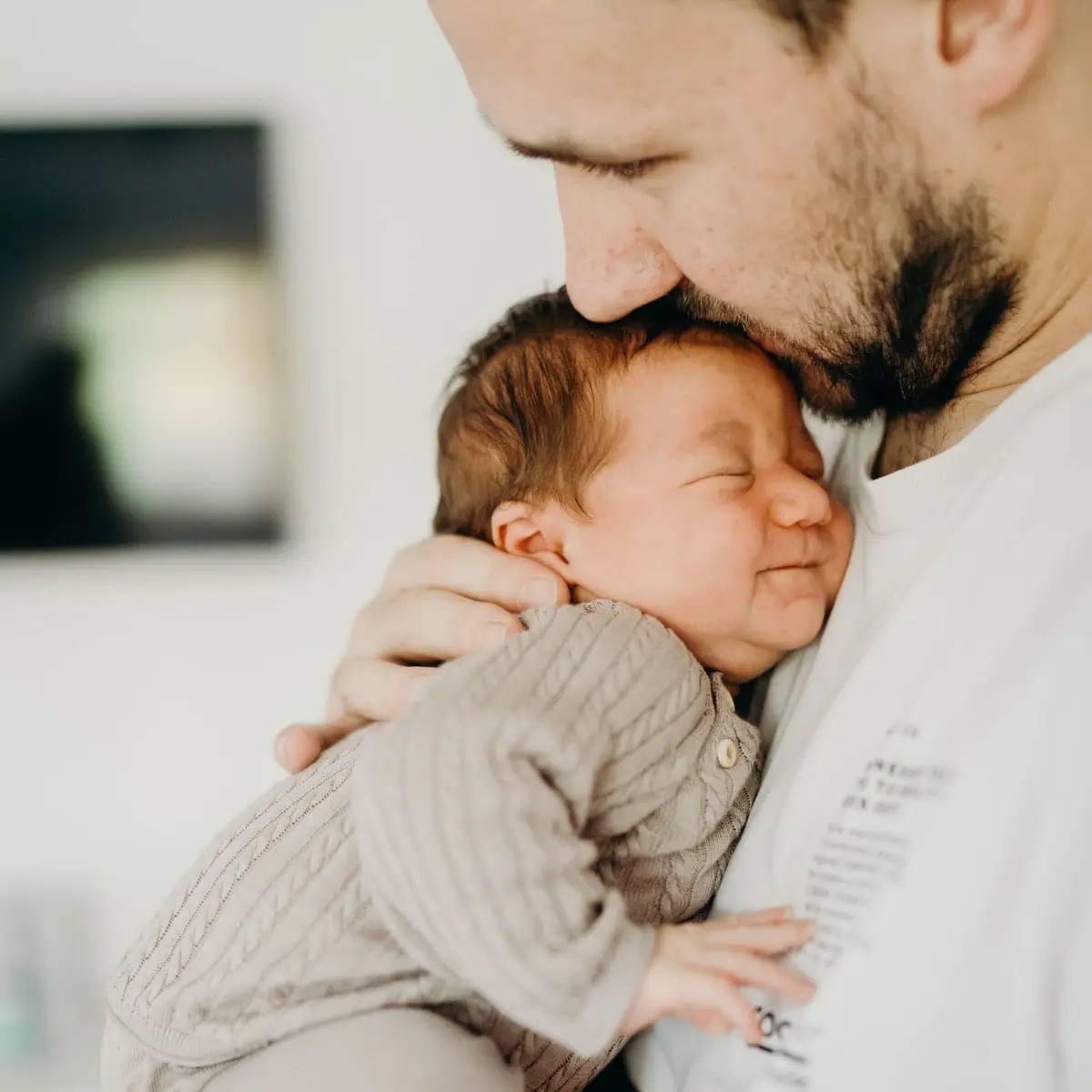 Vater drückt das schlafende Neugeborene an seine Wange, das Baby lächelt